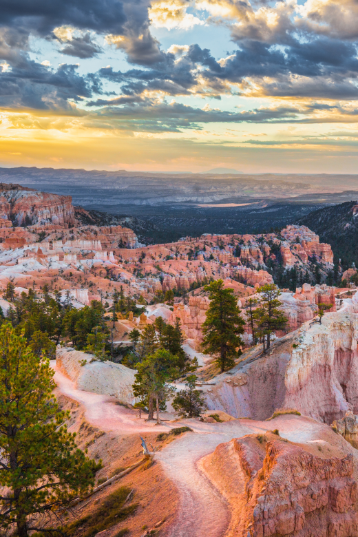 hoodoos and hillsides of bryce canyon national park at sunset. the hills are orange and the sky is golden and blue