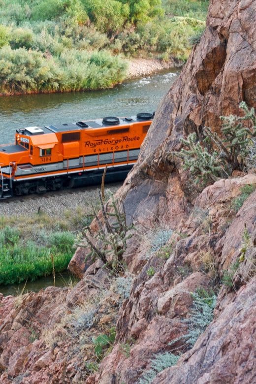 orange train passing by mountain below the Royal Gorge Bridge