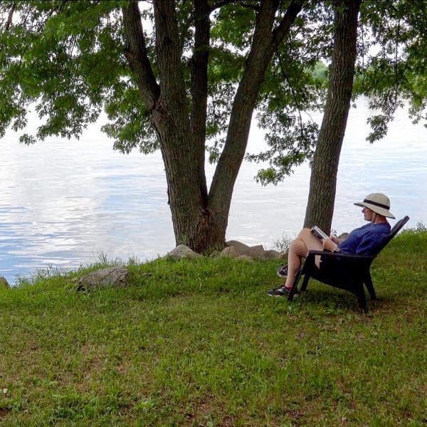 Bev sitting by lake reading book in chair at Round Lake Vineyards, the best Minnesota winery