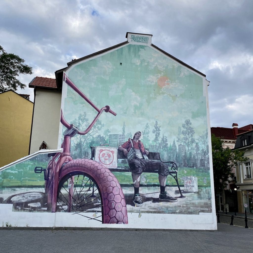 mural of man sitting on bench with bike in foreground
