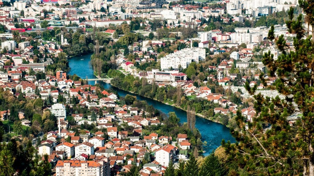 a drone view of the city with white houses and a blue river running through