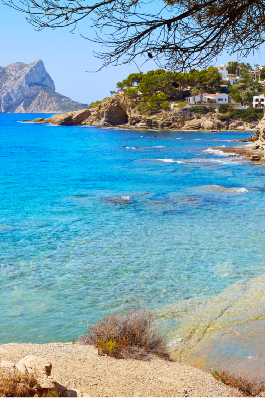 Cala Pinets Beach in Alicante, Spain with deep blue water and sandy beach.