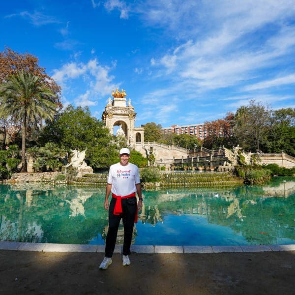 Man standing in front of large pool with statues in a park in Barcelona, Spain
