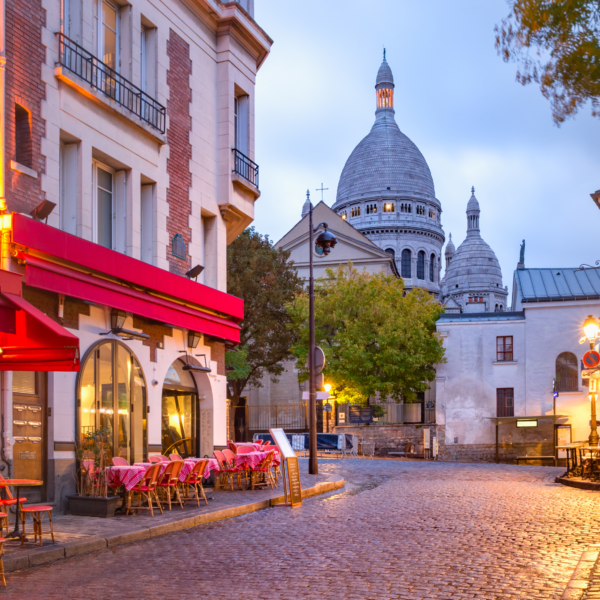 Cobblestone Street in Paris with streetlights, restaurants, and church in background